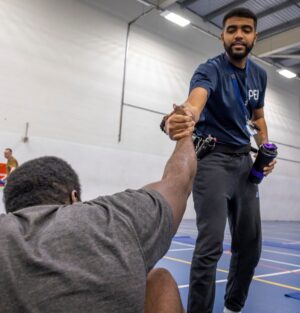 Prison officer in uniform standing and reaching down to help a prisoner up from the ground, firm grasp of hand