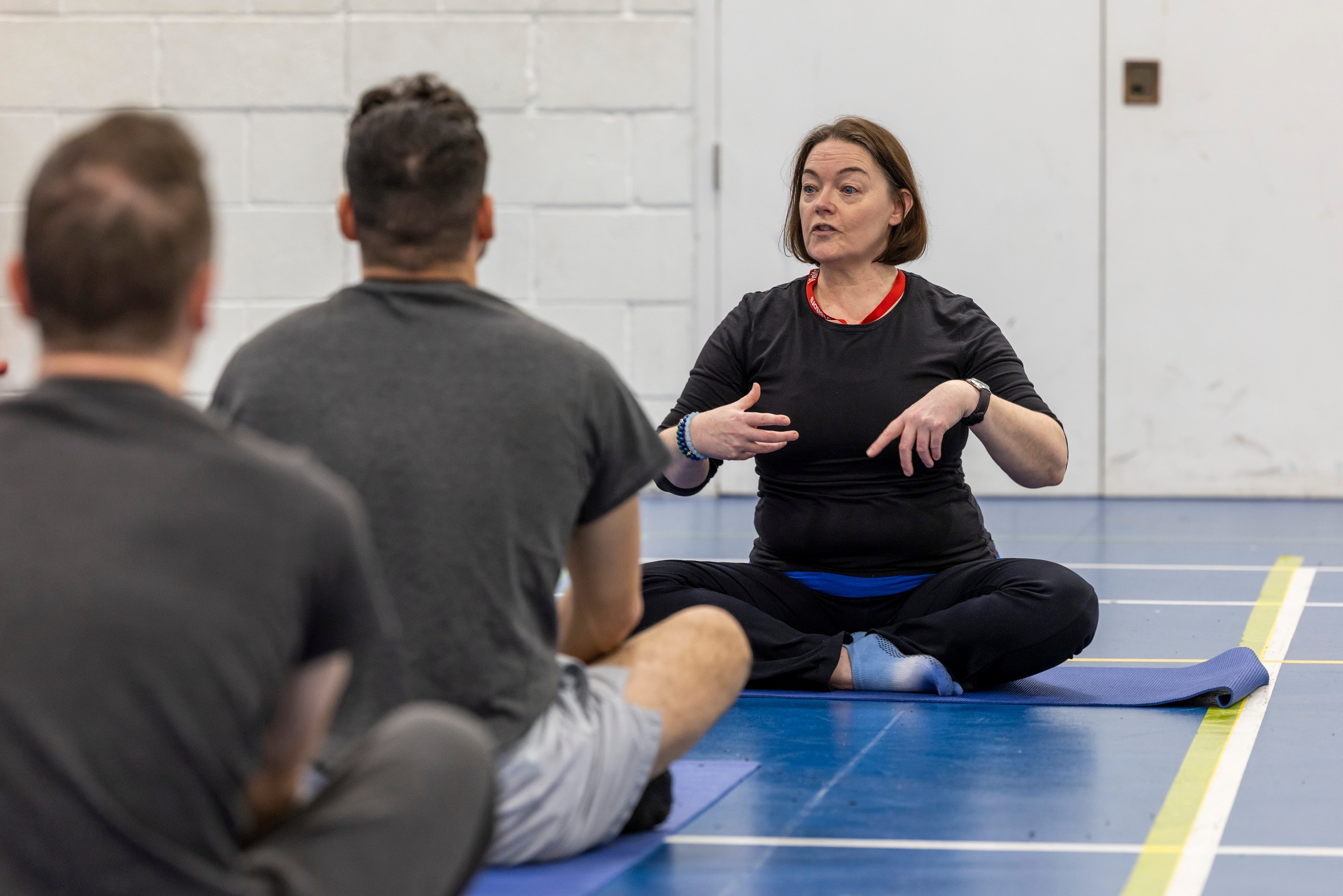 Female yoga teacher sitting cross-legged in gym class for prolific offenders