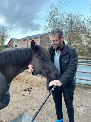Bearded man ibn dark jacket petting a horse