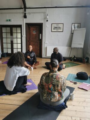 Group of 4 yoga teachers, various ages, sexes and ethnicities, sitting on yoga mats in sunny room