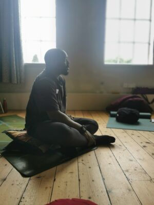 Male yoga teacher of colour sitting on mat in a sunny room.