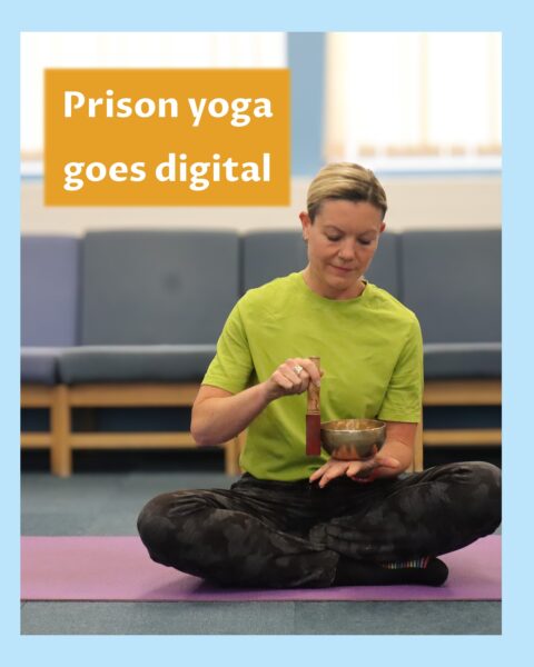 Fair haired woman sitting cross-legged on yoga mat in a prison gym looking down at a singing bowl