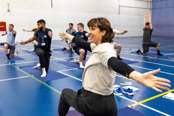 In a prison gym, female teacher with arms outstretched and students following her instructions