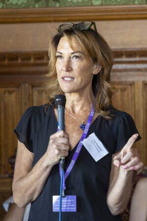 Lisa Newman, PPT ambassador in black top holding microphone at event in the River Rooms in the House of Lords